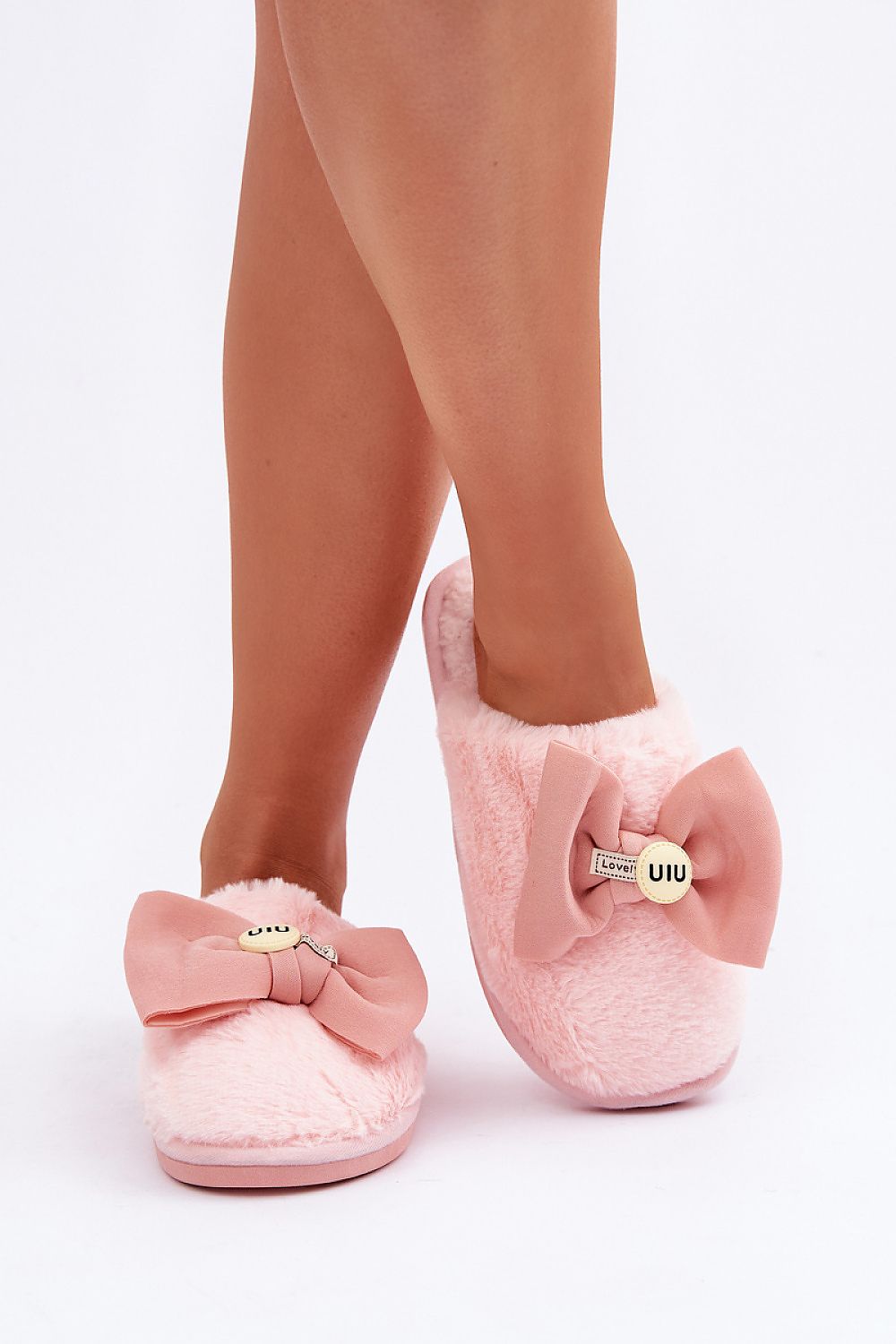 Pink slippers with bow details worn by a person on a white background
