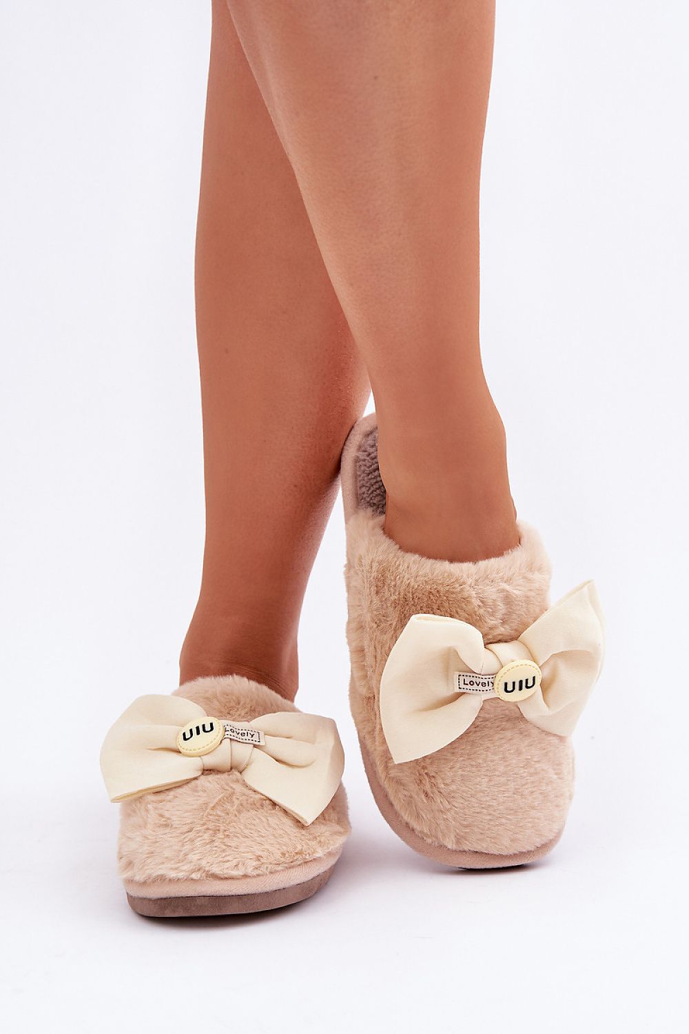 Beige slippers with bow details worn by a person on a white background