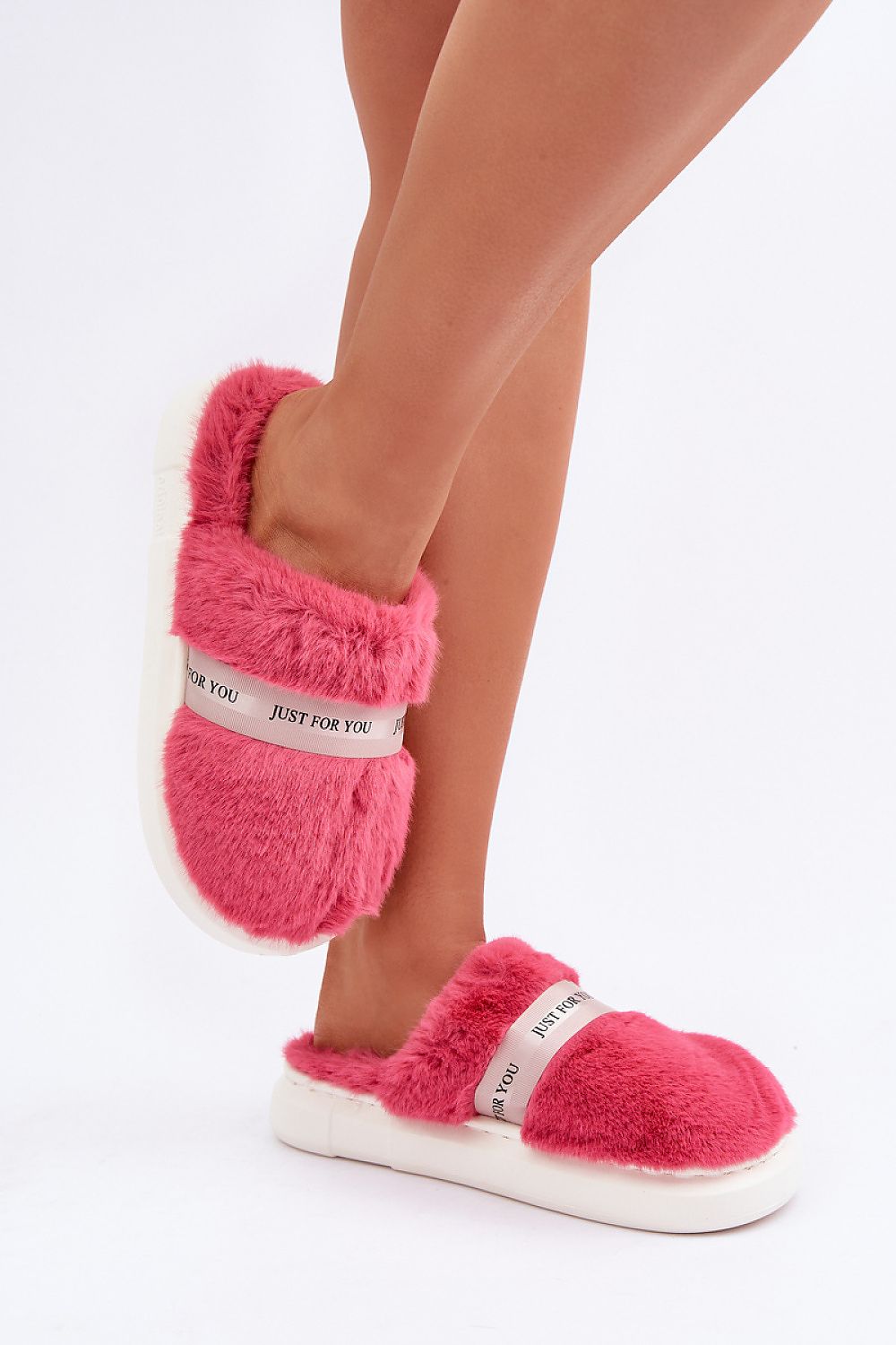 Pink fuzzy slippers with white sole worn by a person on a light gray background