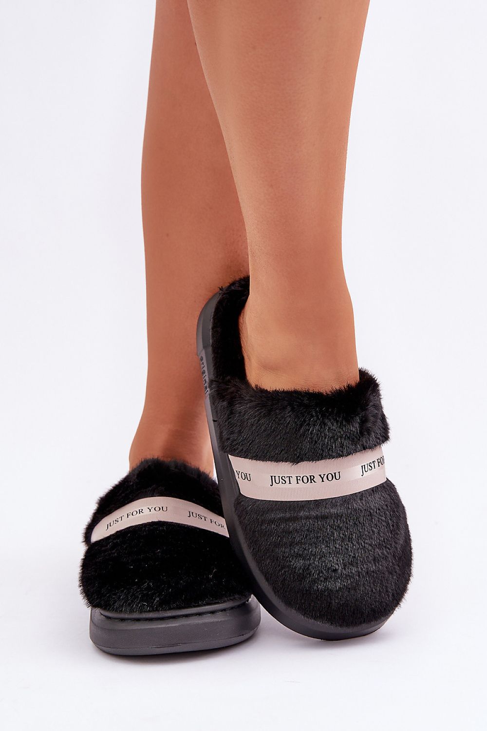 Black slippers with fur trim worn by a person on a white background