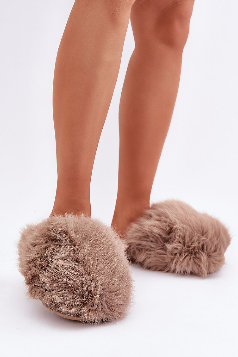 Brown fuzzy slippers worn with beige tights on a white background