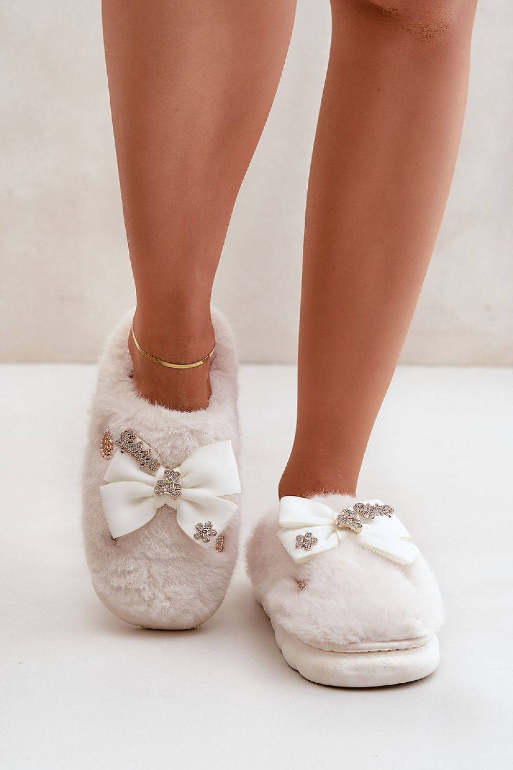 White fluffy slippers with decorative bows and crystals on a neutral background