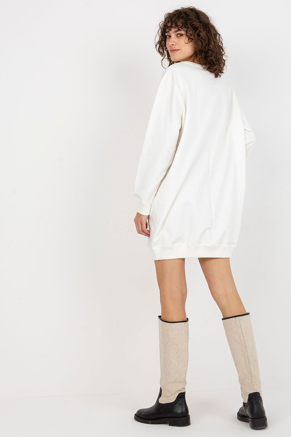 Person wearing a white sweater dress with knee-high socks and black shoes on a white background