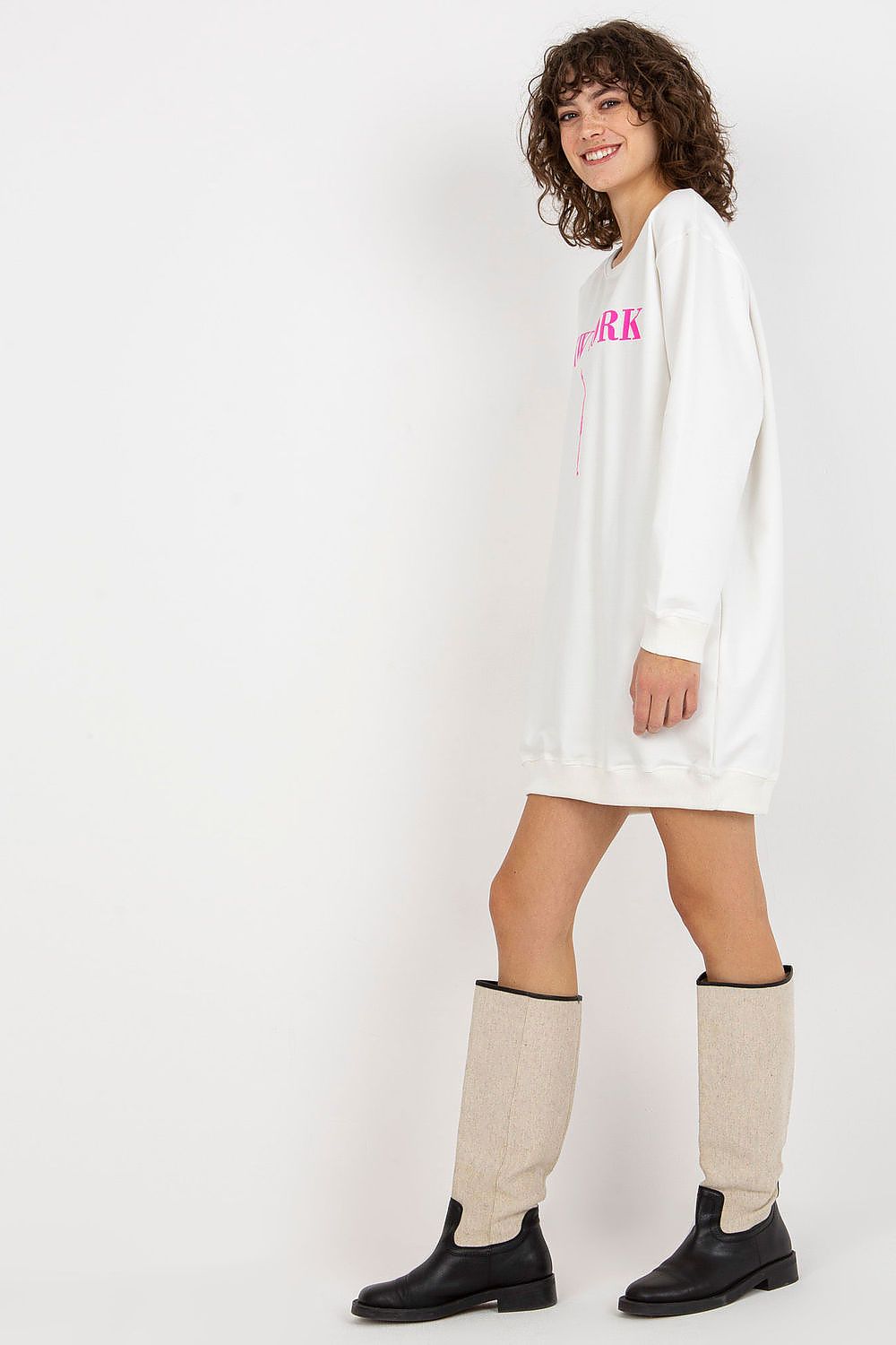 Woman wearing a white oversized hoodie dress with pink text and knee-high boots on a white background