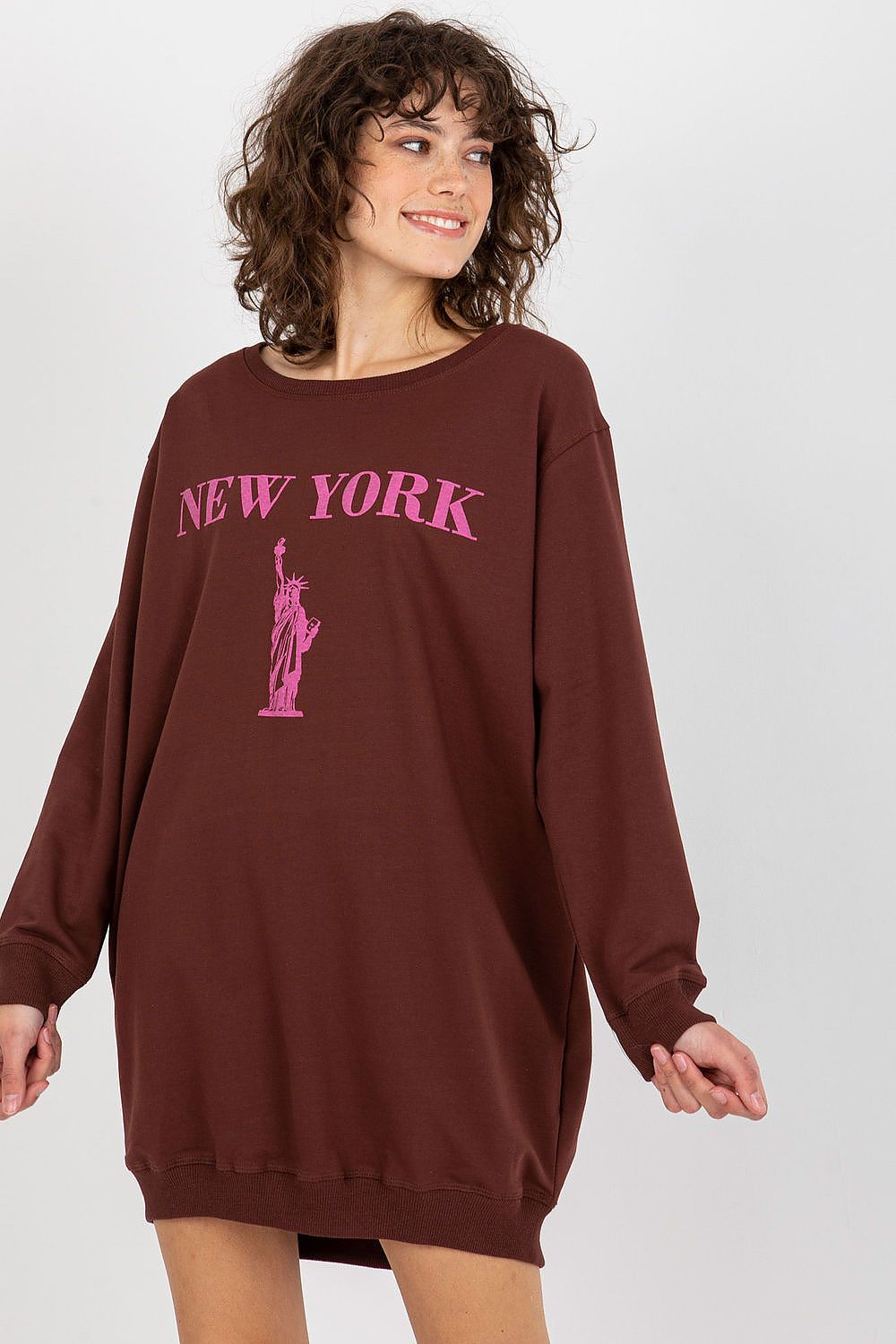 Woman wearing a brown sweatshirt with 'New York' and Statue of Liberty graphic on a plain background
