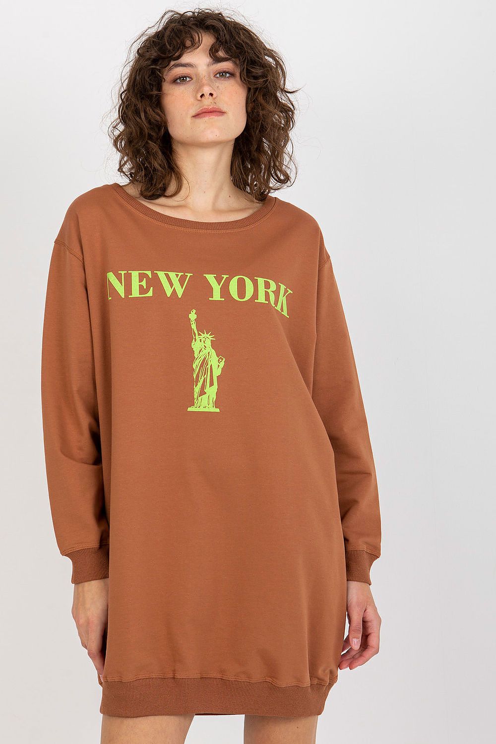Woman wearing a brown sweatshirt dress with 'New York' and Statue of Liberty graphic on a white background