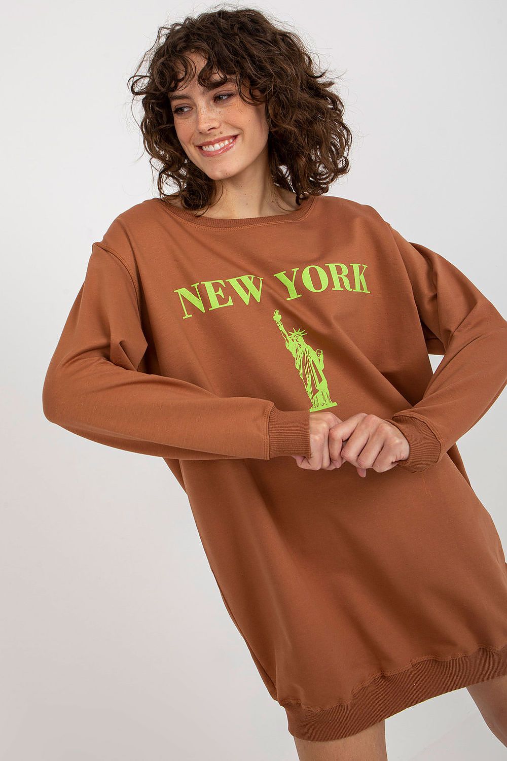 Woman wearing a brown sweatshirt with 'New York' and Statue of Liberty graphic on a white background