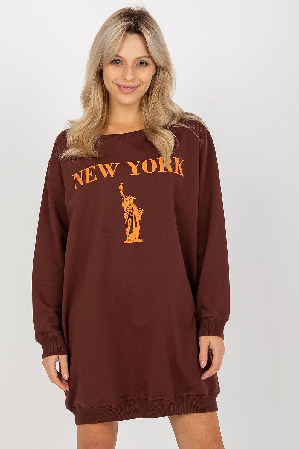 Woman wearing a brown sweatshirt dress with 'New York' and Statue of Liberty print on a white background