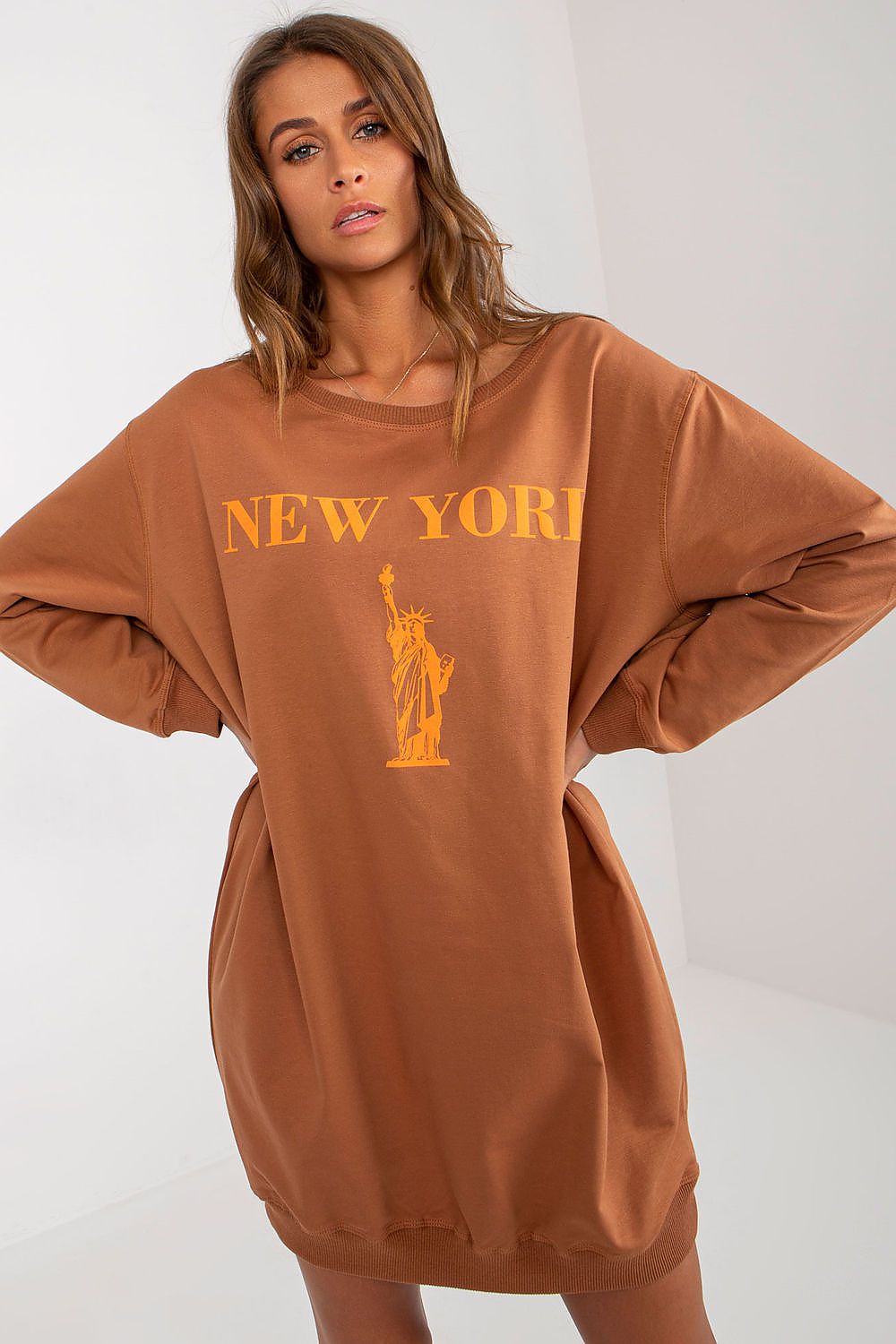 Woman wearing a brown sweatshirt with 'New York' and Statue of Liberty graphic on a white background