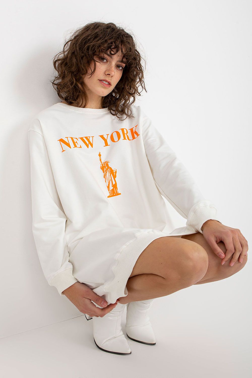 Woman wearing a white sweatshirt with 'New York' and a statue of liberty graphic on a white background