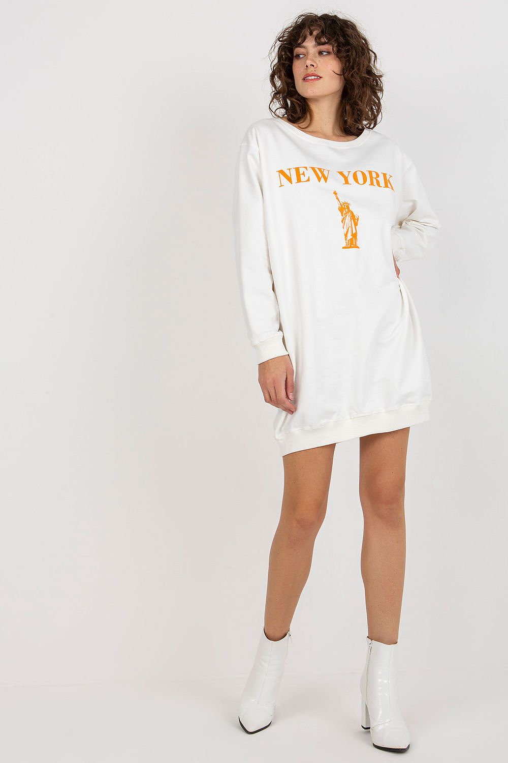 Woman wearing a white sweatshirt dress with 'New York' print and white boots on a light gray background