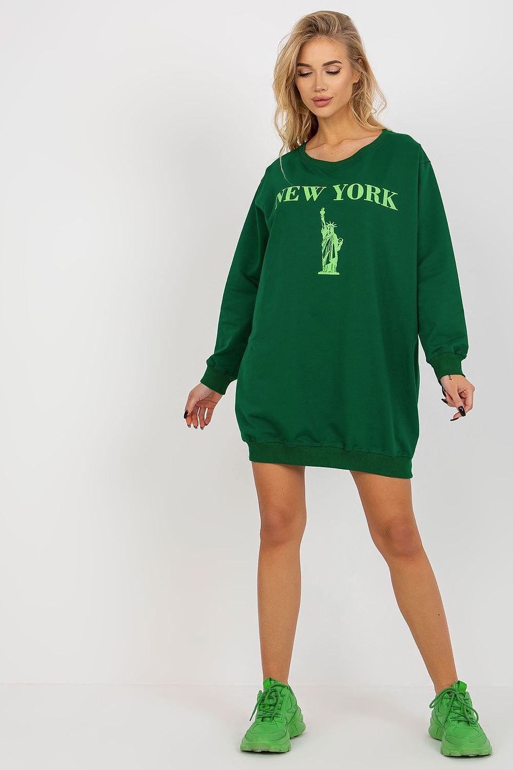 Woman wearing a green sweatshirt dress with 'New York' and Statue of Liberty graphic on a white background