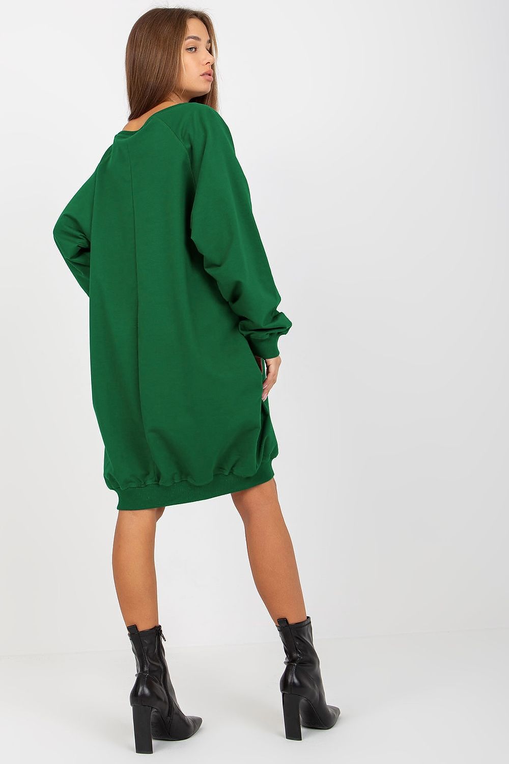 Woman wearing a green oversized sweatshirt dress with black boots on a white background