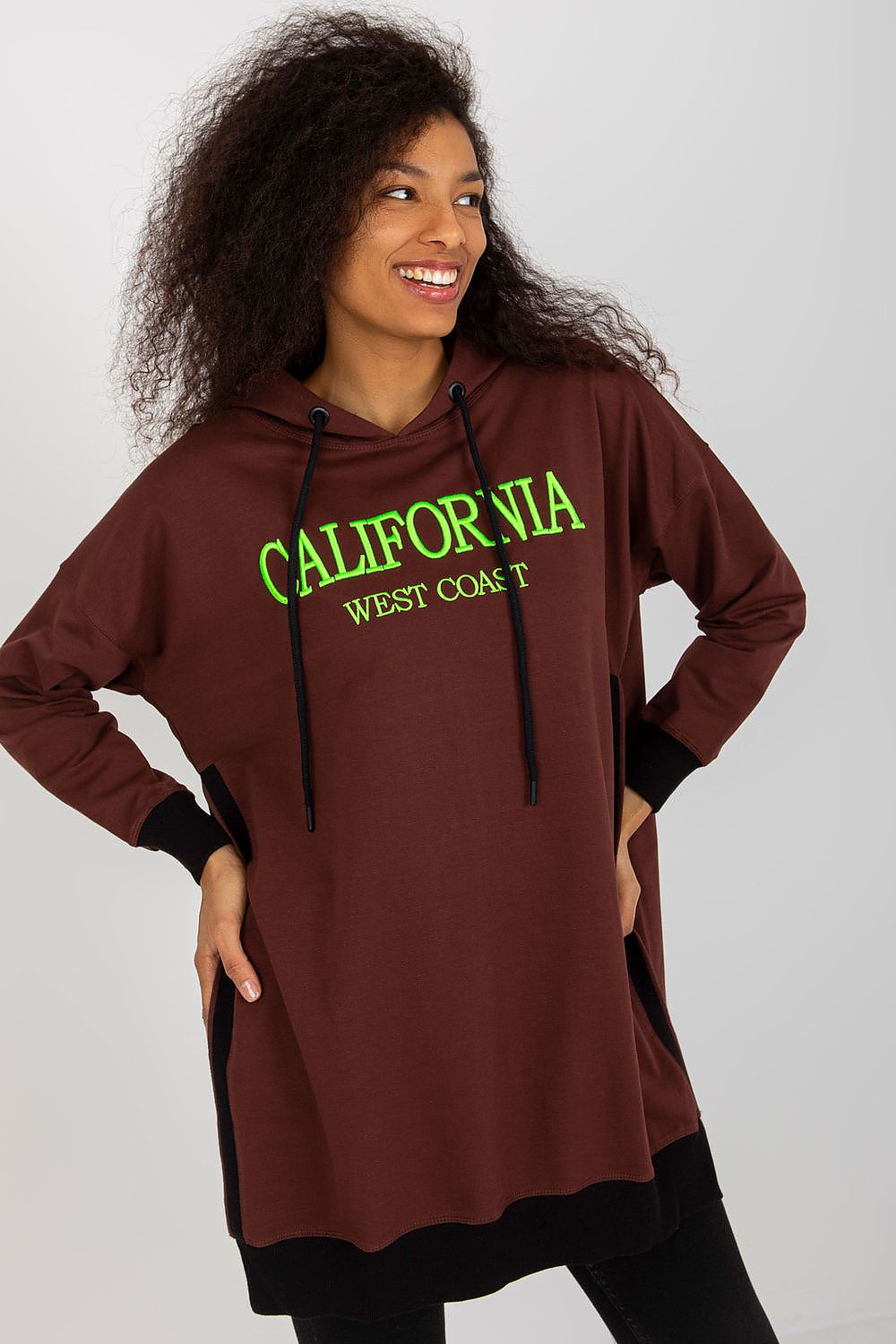 Woman wearing a brown hoodie with 'California West Come T' text on a white background