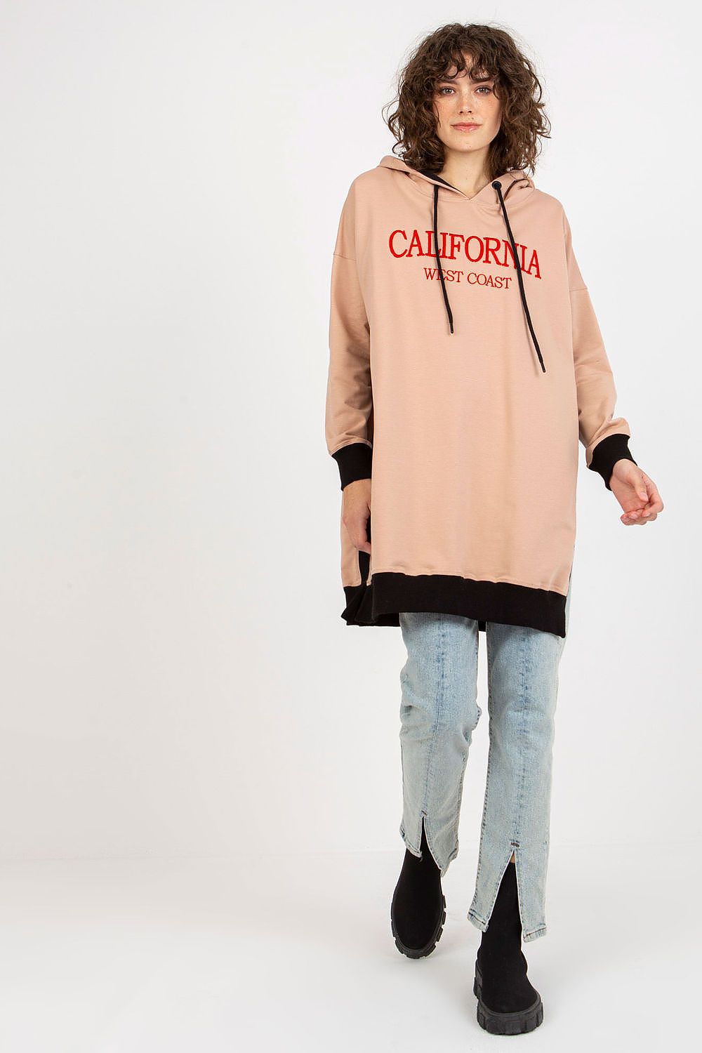 Person wearing a beige hoodie with red text and light blue jeans on a white background