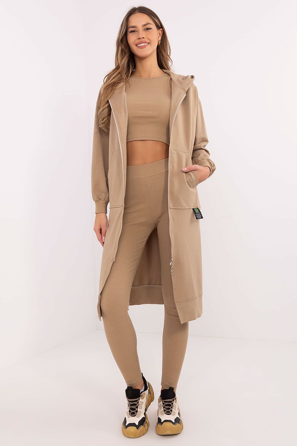 Woman wearing a beige outfit with a long coat on a white background