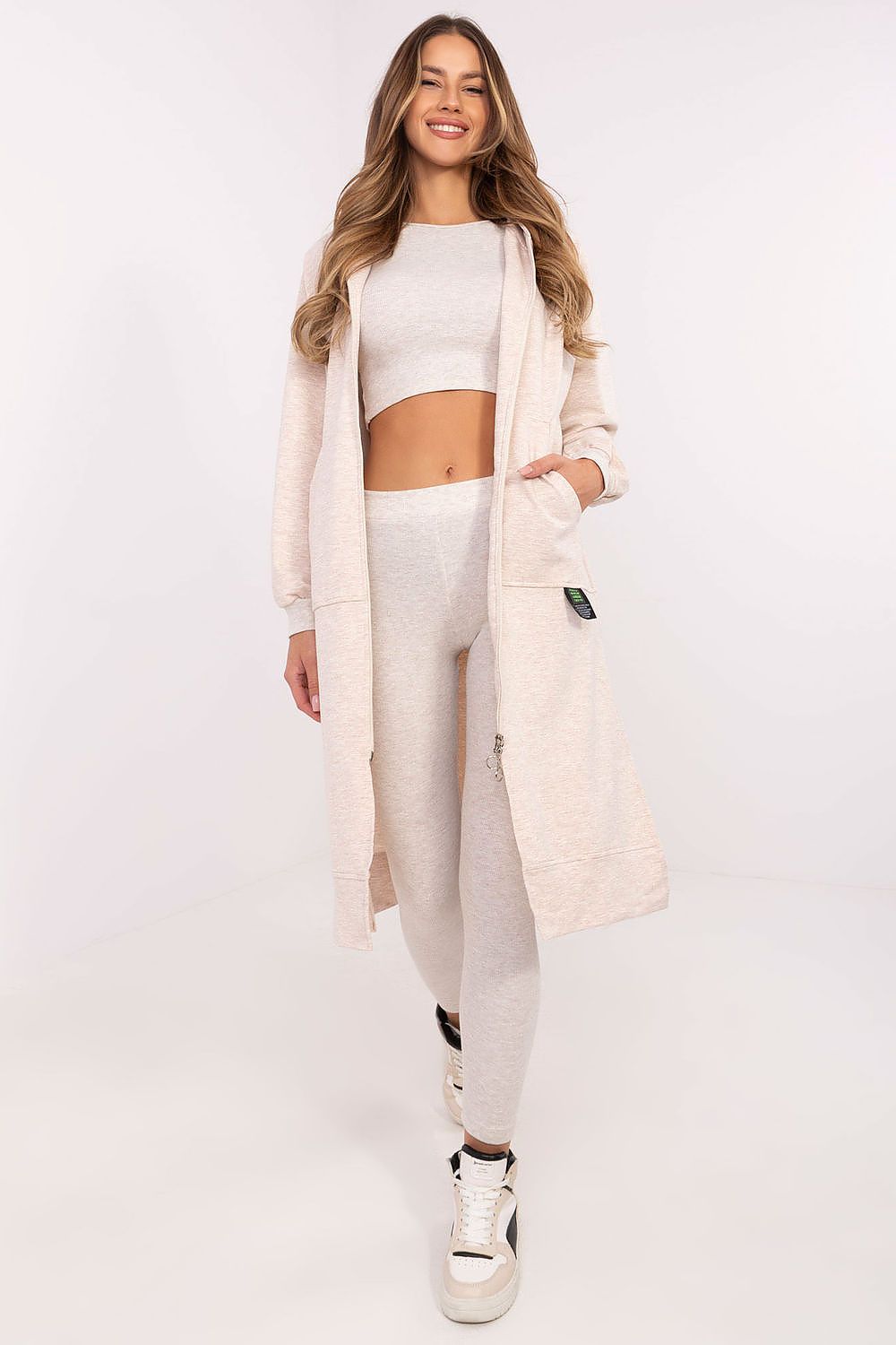 Woman wearing a beige long cardigan, white top, and pants on a white background