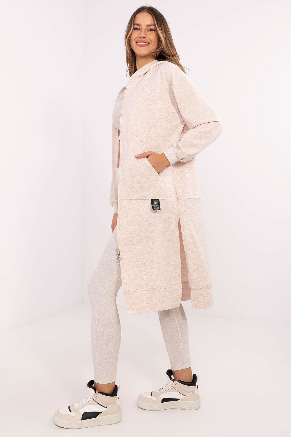 Woman wearing a beige long coat, white pants, and black shoes on a white background