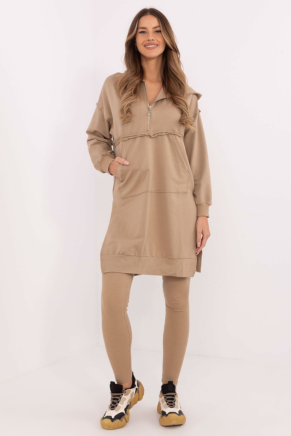 Woman wearing a beige hoodie dress and leggings on a white background