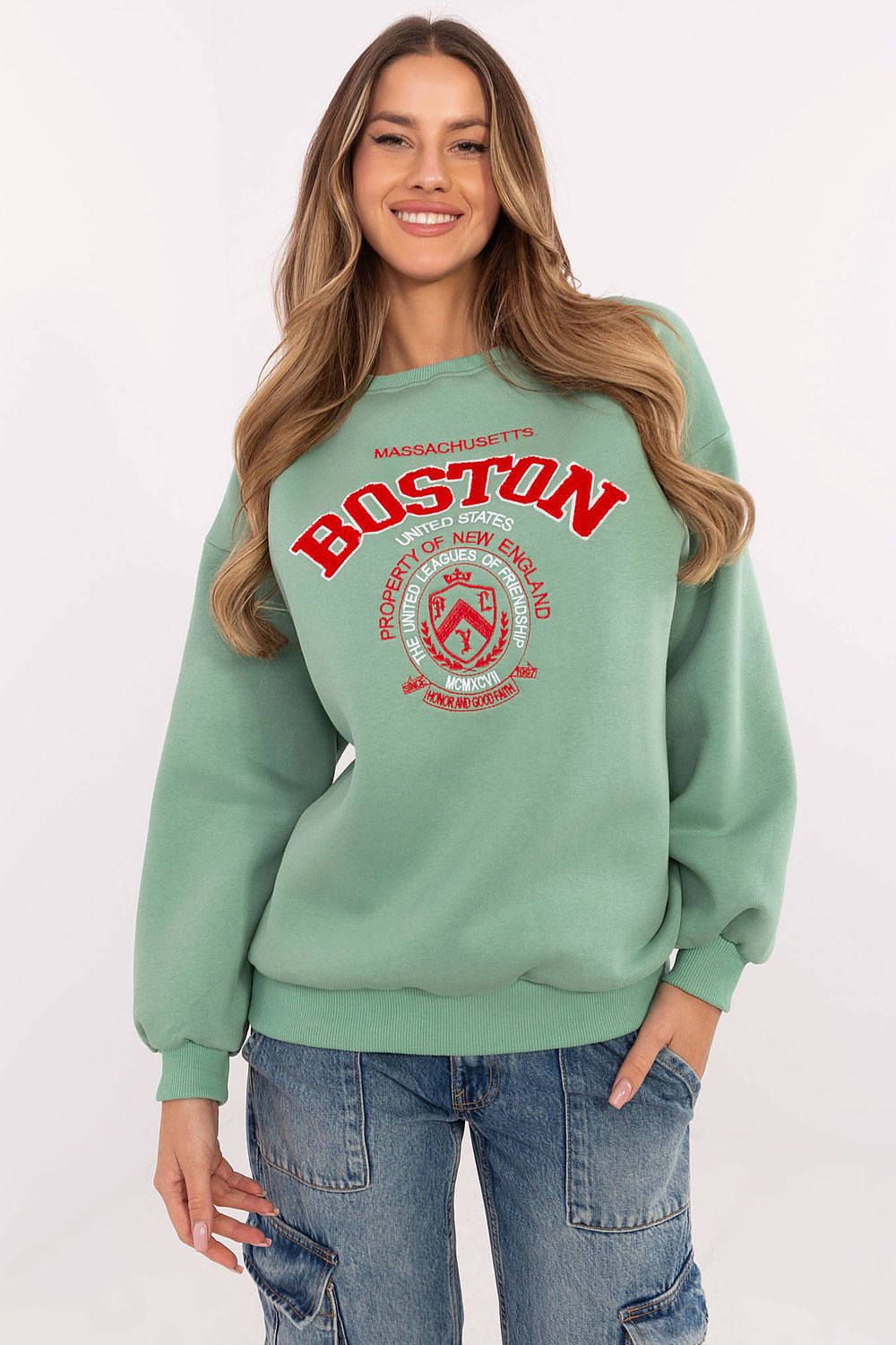 Woman wearing a green sweatshirt with 'Boston' printed on it against a white background