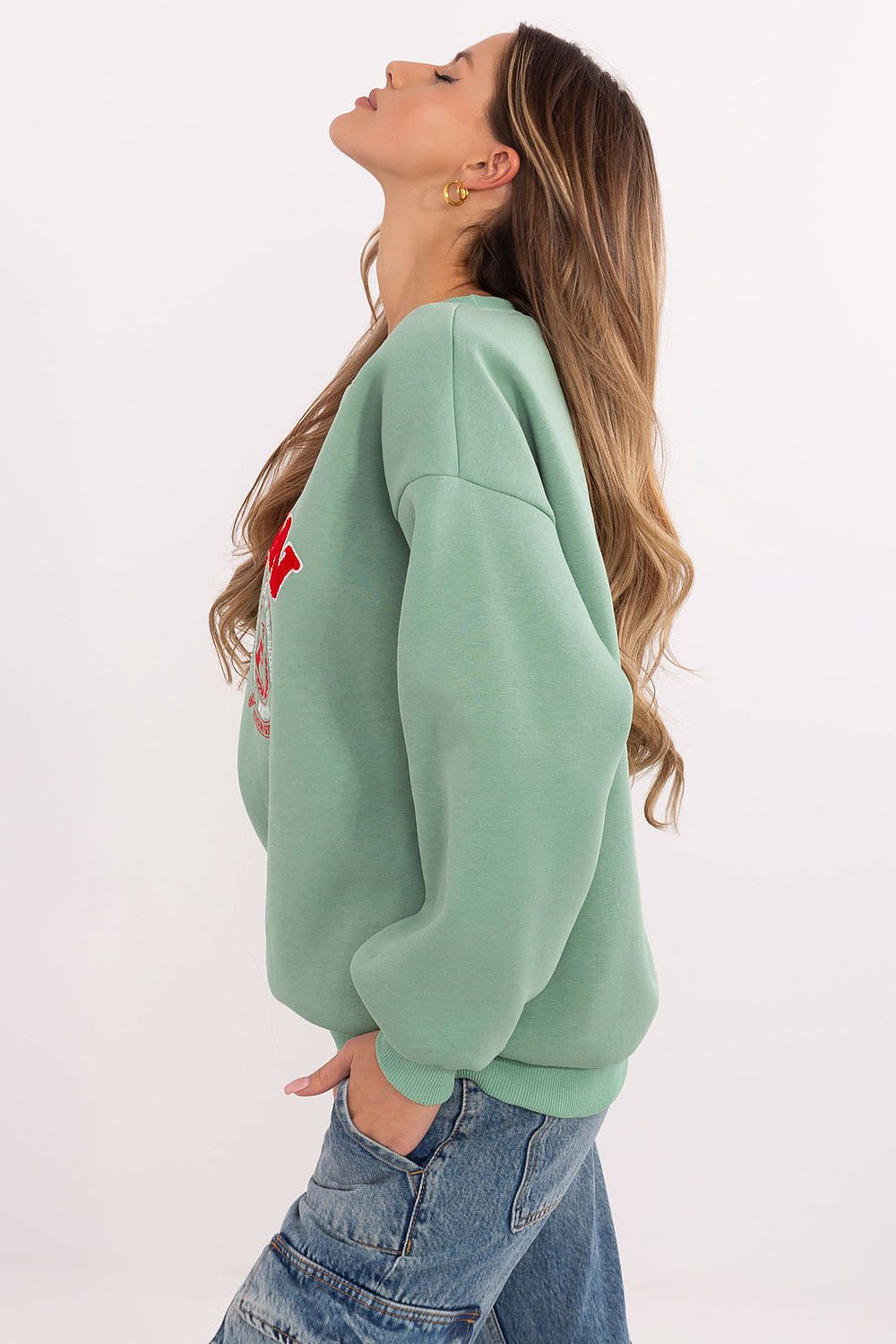 Woman wearing a light green sweatshirt with a red design on the back against a white background