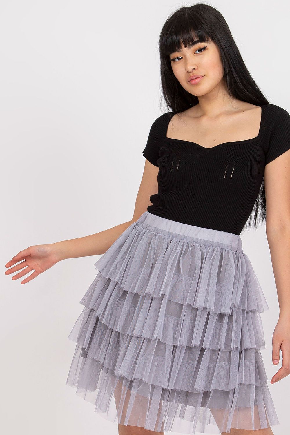 Woman wearing a black top and gray tiered skirt on a white background