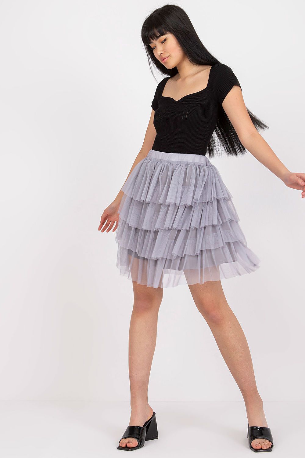 Woman wearing a black top and gray tiered skirt on a white background