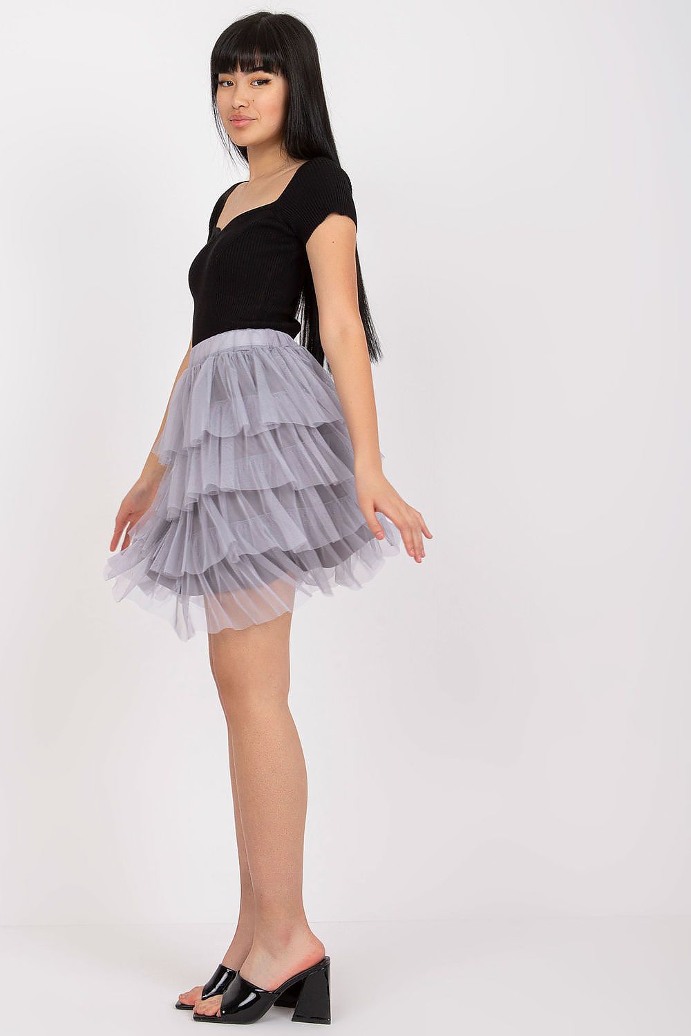 Woman wearing a black top and layered gray skirt on a white background