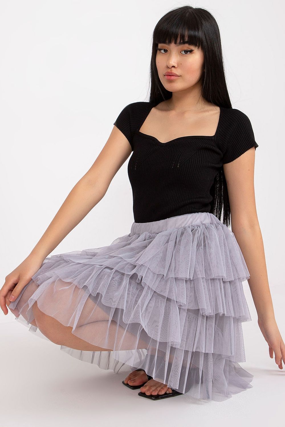 Woman wearing a black top and layered gray skirt on a white background