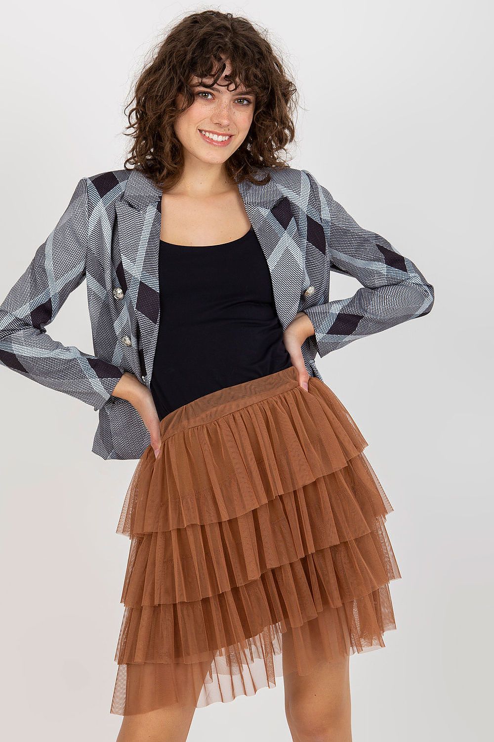 Woman wearing a plaid jacket, black top, and brown tiered skirt on a white background