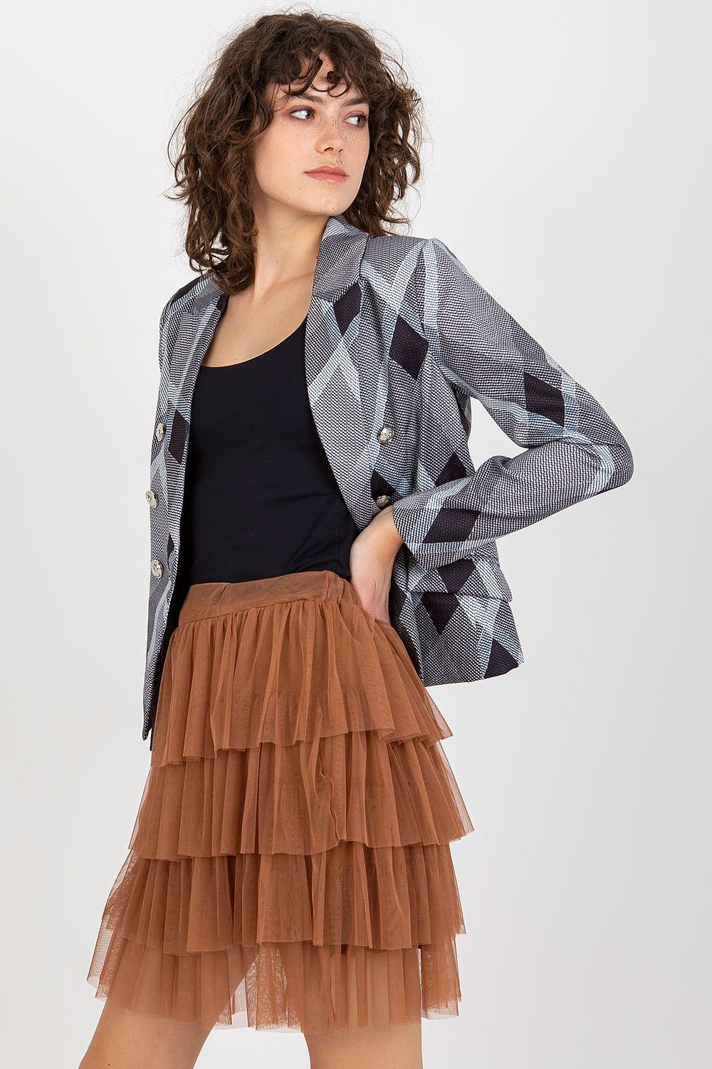Woman wearing a patterned blazer, black top, and brown tiered skirt on a white background