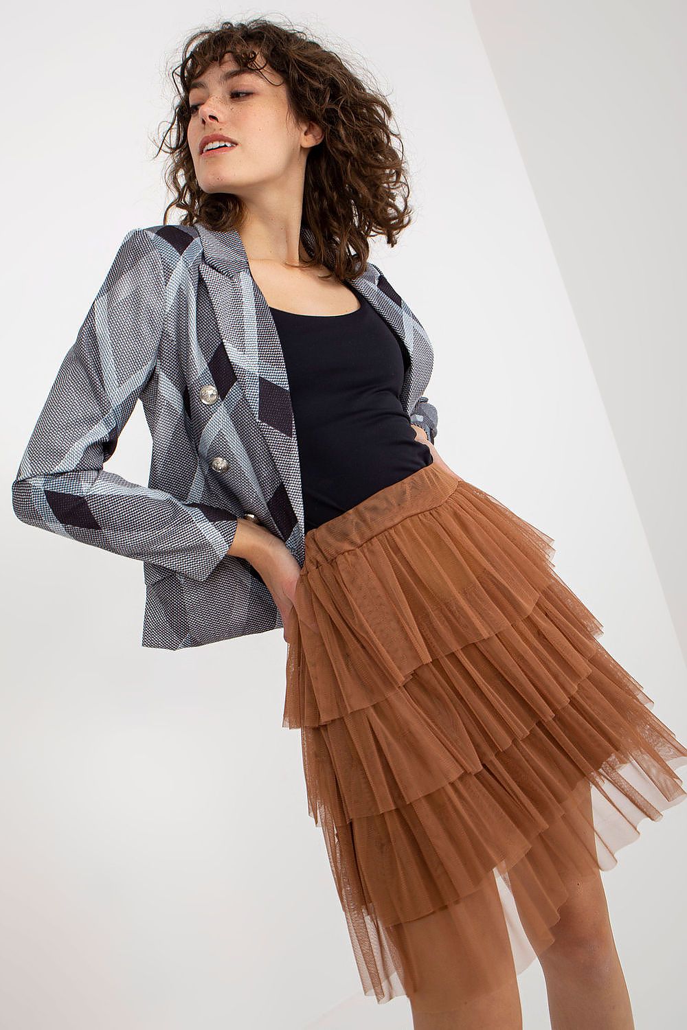 Woman wearing a plaid jacket, black top, and brown tiered skirt on a white background