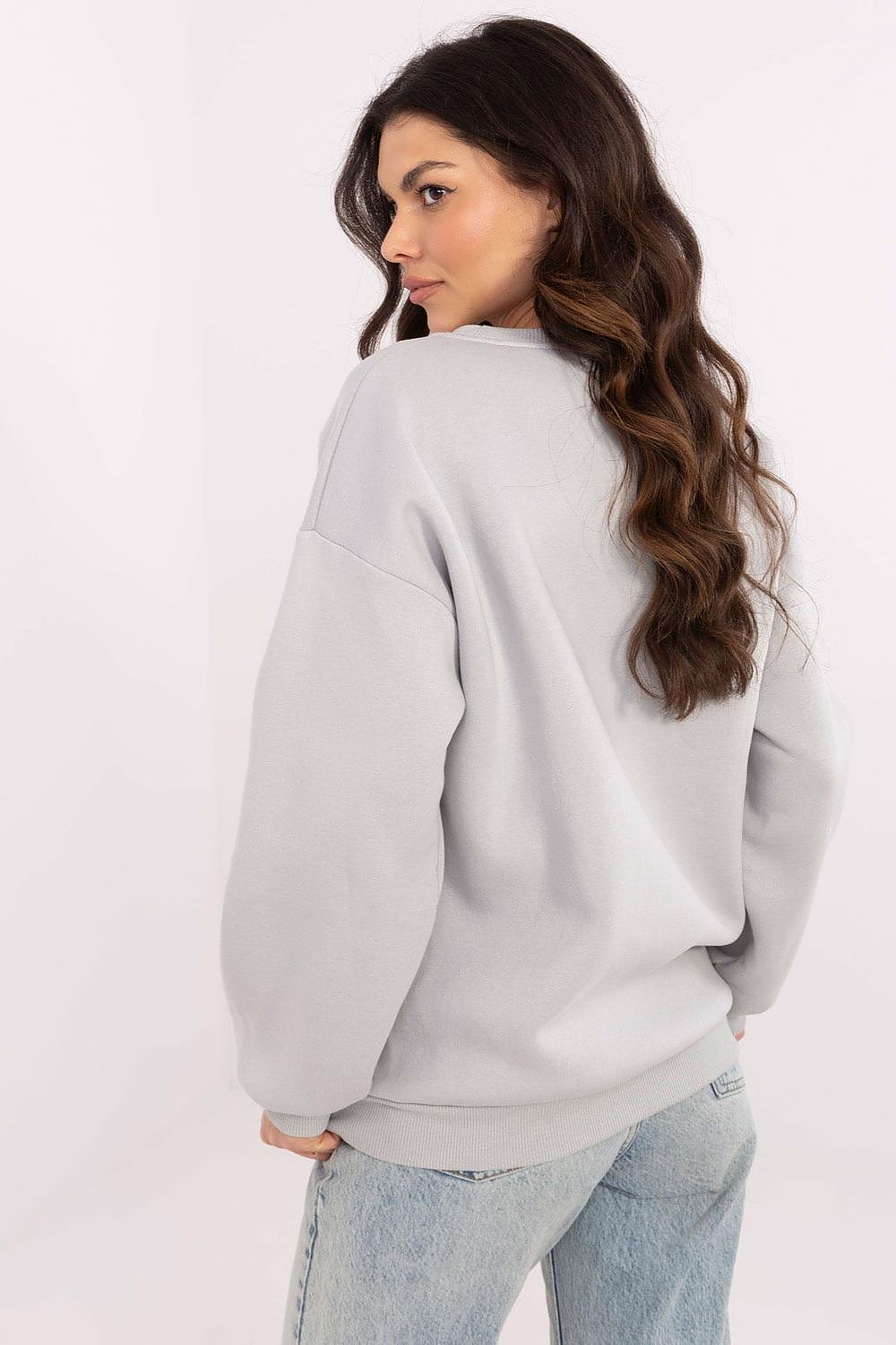 Woman wearing a light gray sweatshirt and light blue jeans on a white background