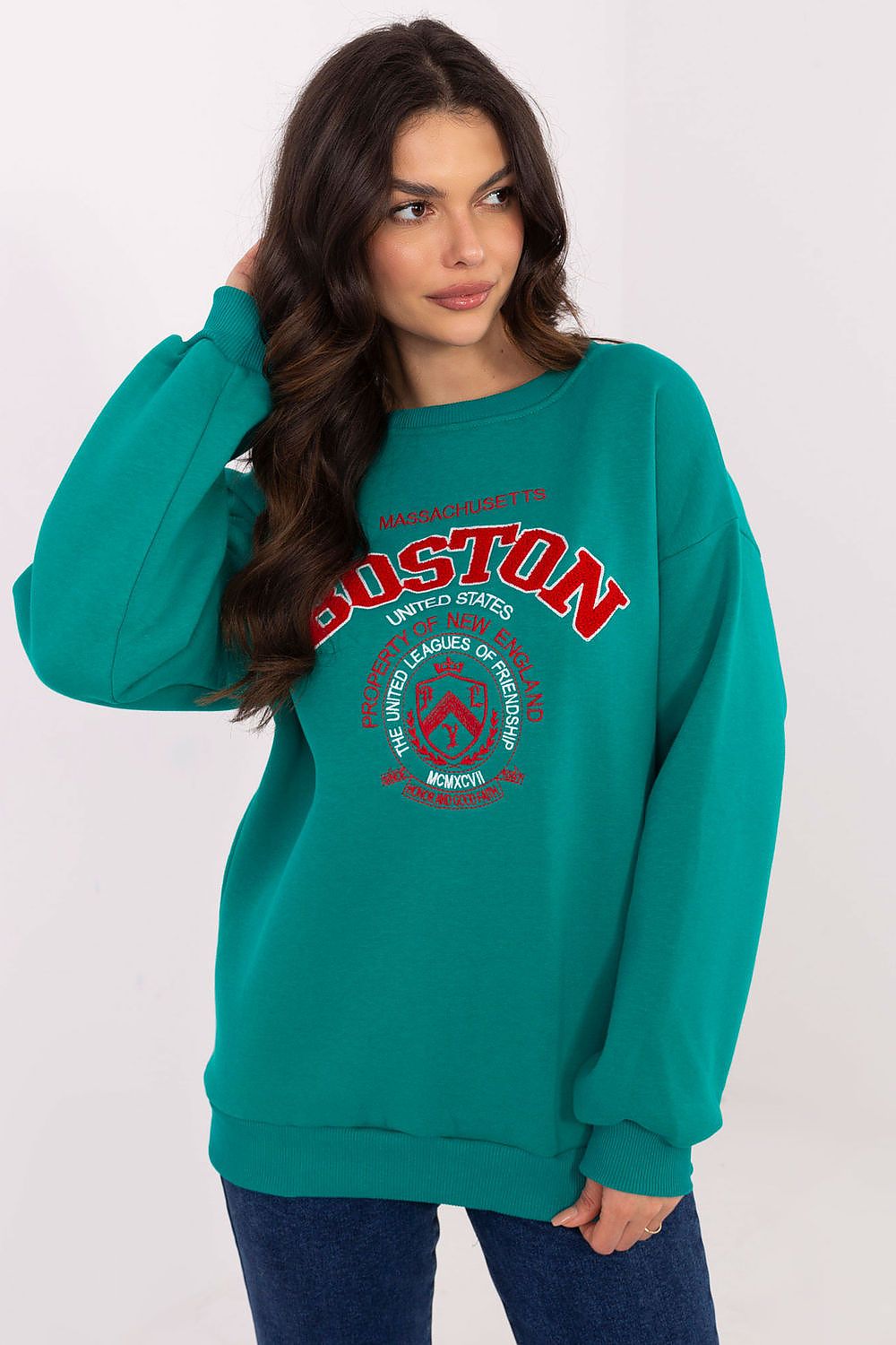 Woman wearing a teal sweatshirt with 'Boston' printed on it against a white background
