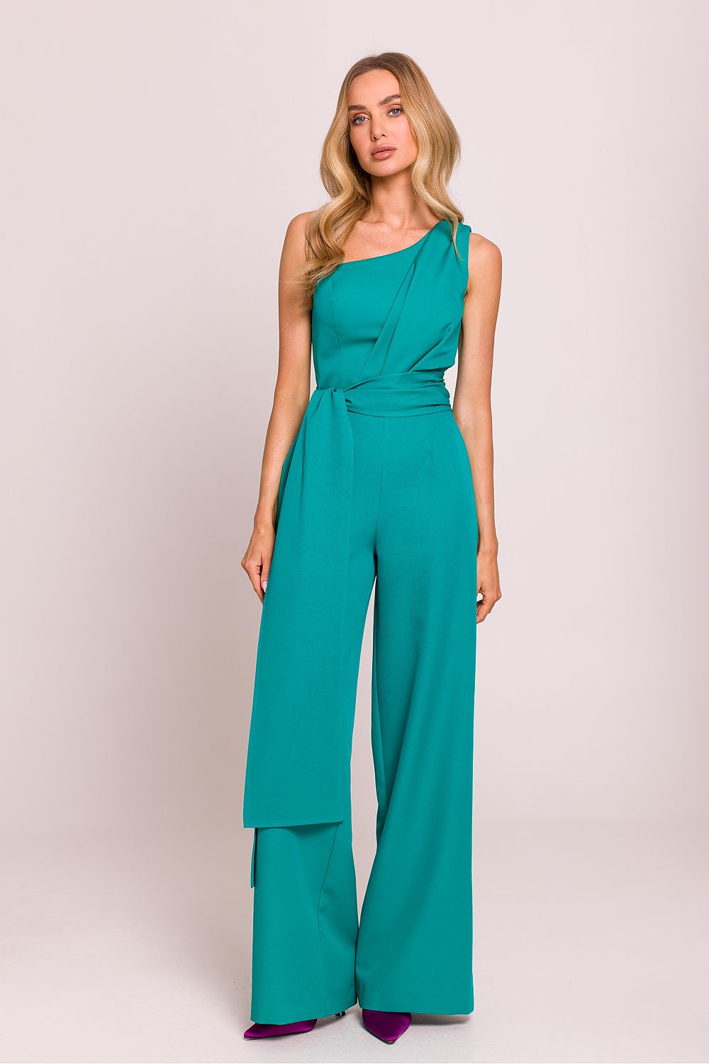 Woman wearing a teal jumpsuit on a plain background