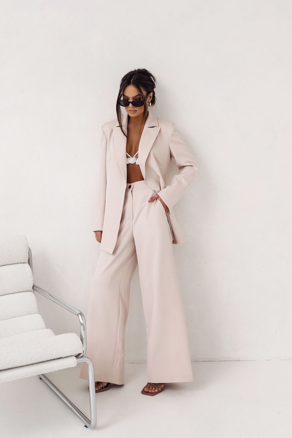 Woman in a beige suit standing in a minimalistic room with white furniture.
