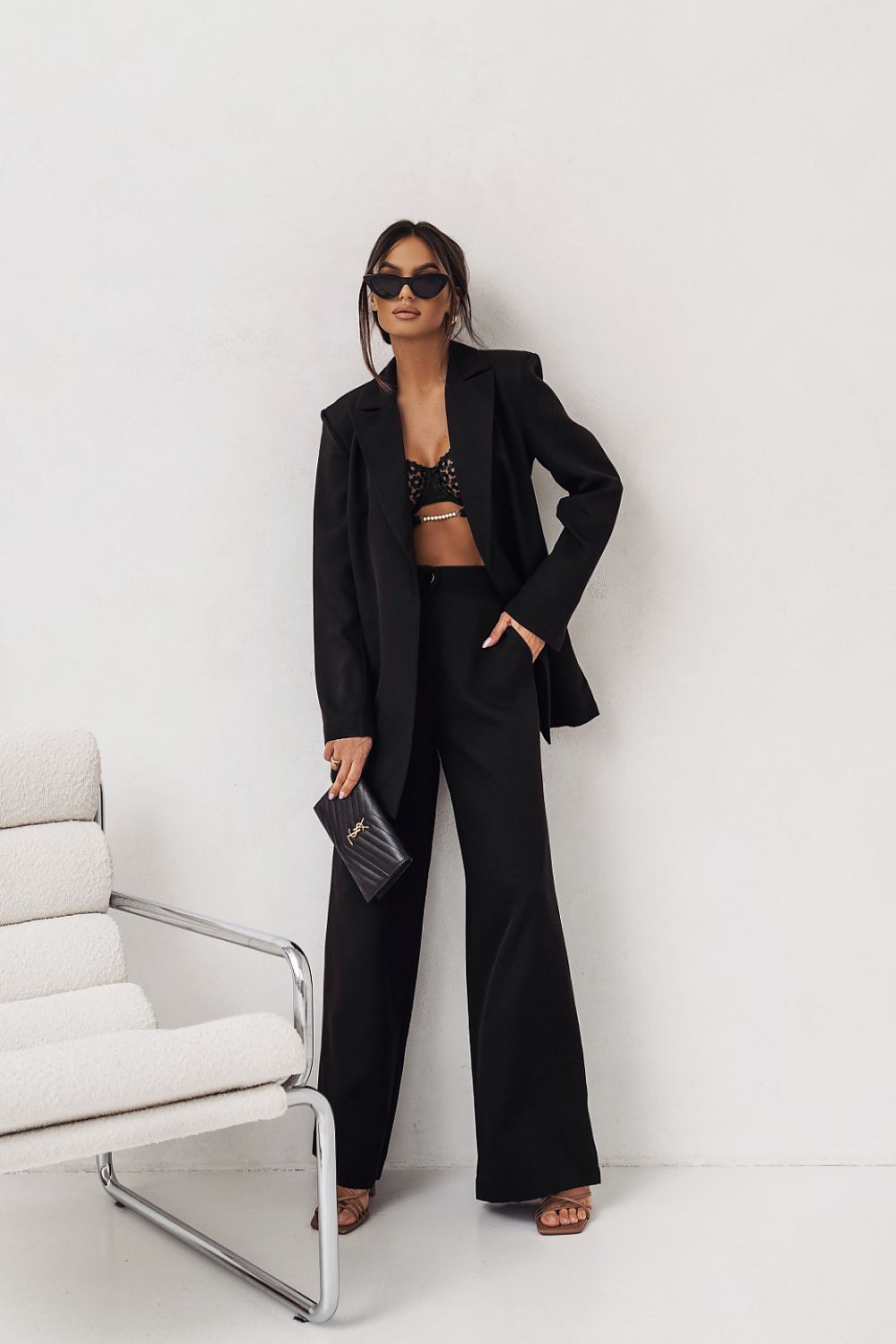 Woman in a black suit standing in a minimalistic room with a white chair.
