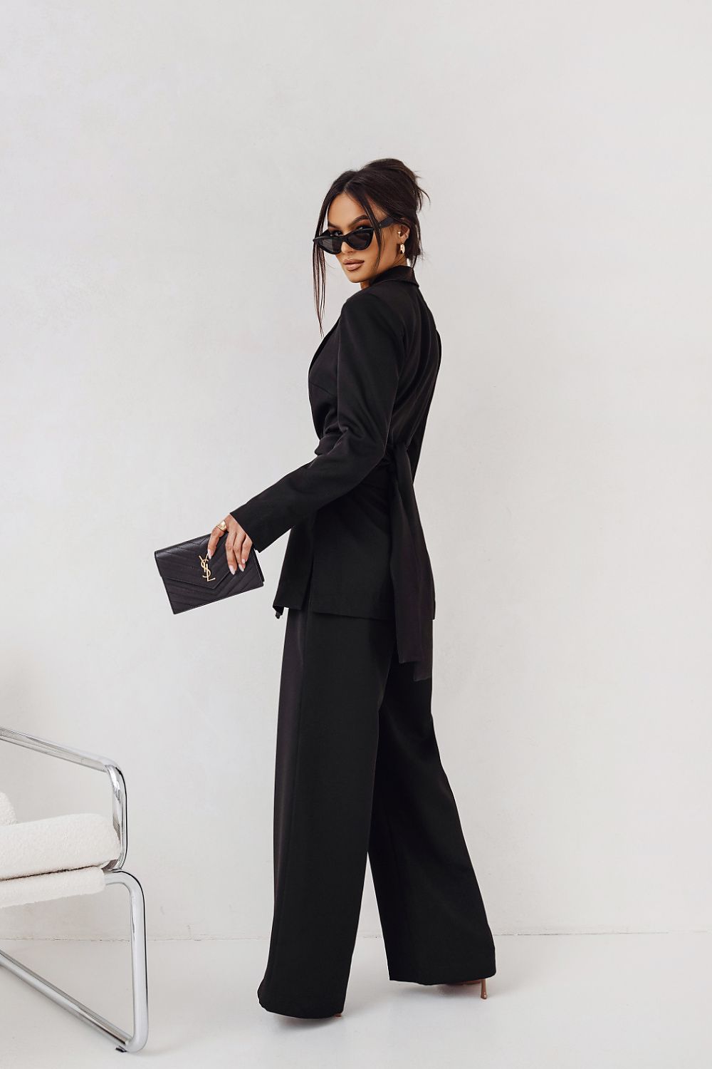 Woman in a black suit holding a clutch against a white background