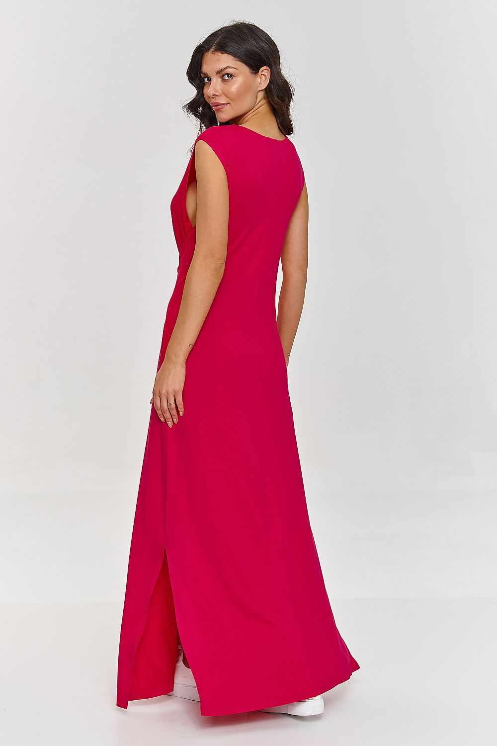 Woman wearing a bright pink sleeveless dress with a slit on a white background
