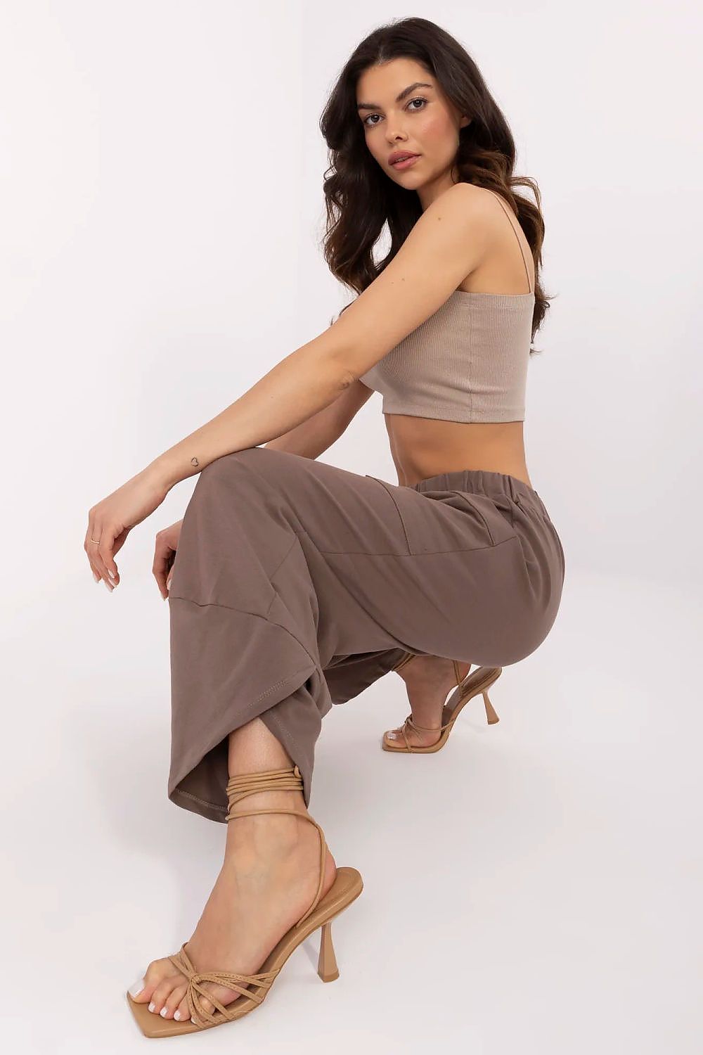 Woman wearing a brown outfit with high-waisted pants and a crop top on a white background