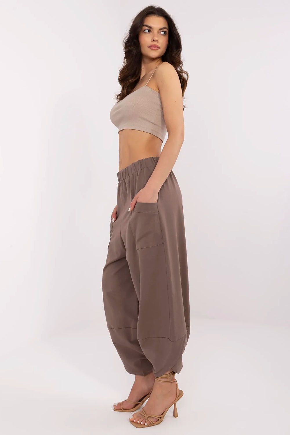 Woman wearing a beige crop top and brown harem pants on a white background
