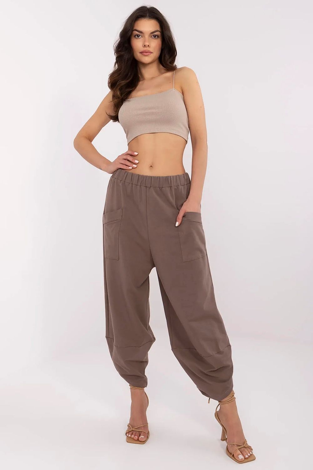 Woman wearing a beige top and brown harem pants on a white background