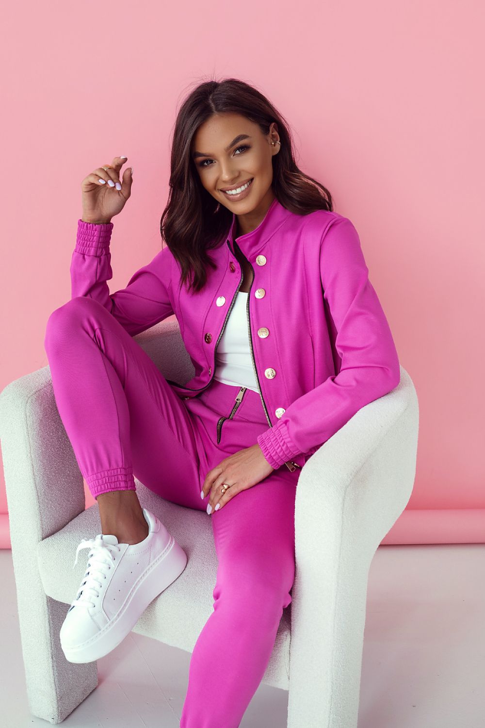 Woman in a bright pink outfit sitting on a white chair against a pink background
