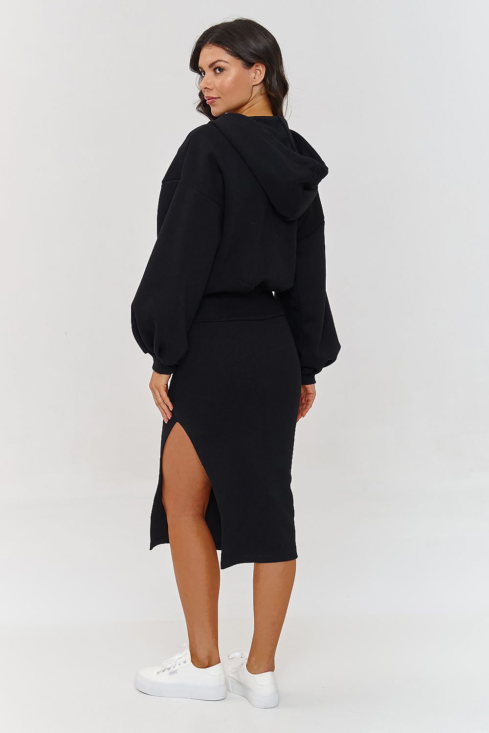 Woman wearing a black hoodie and black skirt with a high slit on a white background