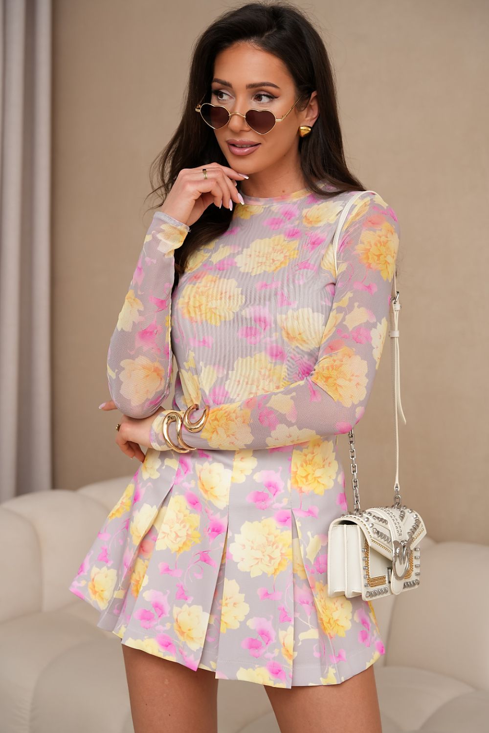 Woman wearing a floral dress with a beige handbag indoors.