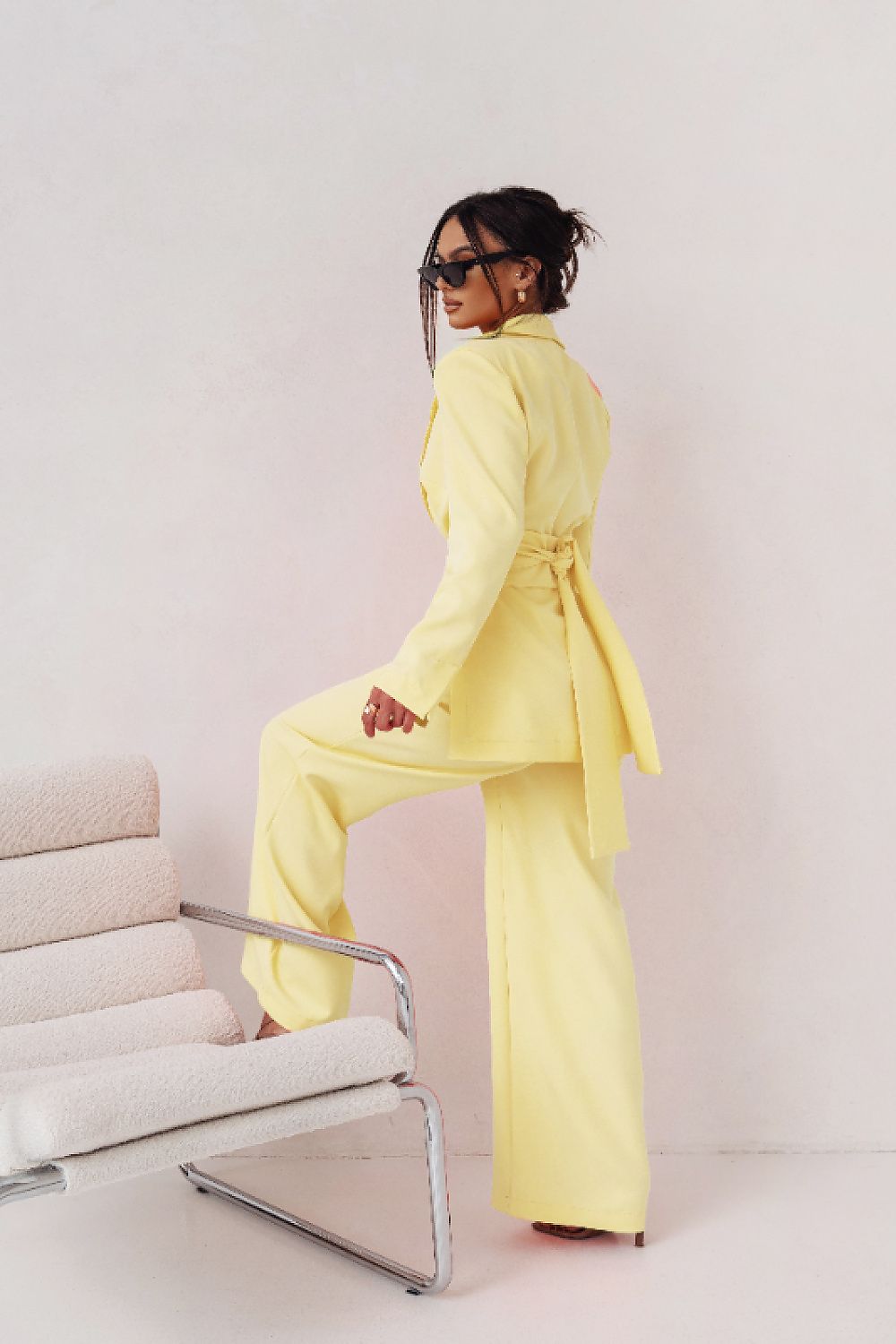 Person wearing a yellow suit sitting on a modern chair against a white background