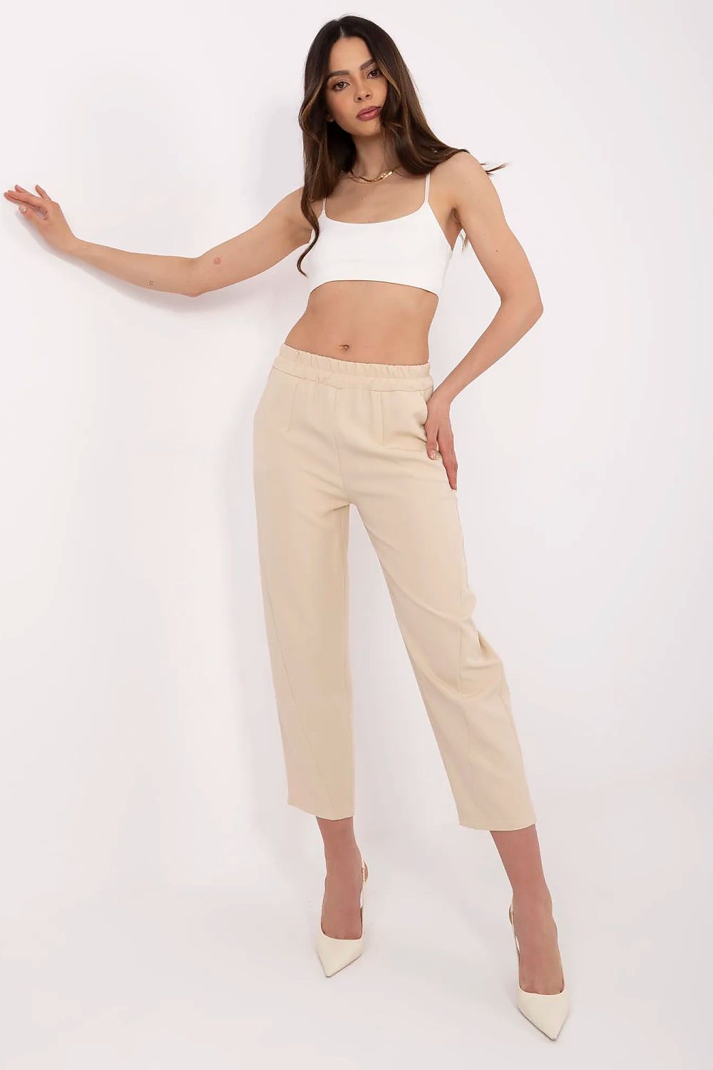 Woman wearing a white crop top and beige pants on a white background