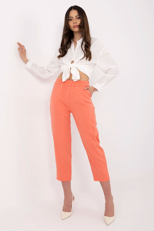 Woman wearing a white blouse and orange pants on a white background