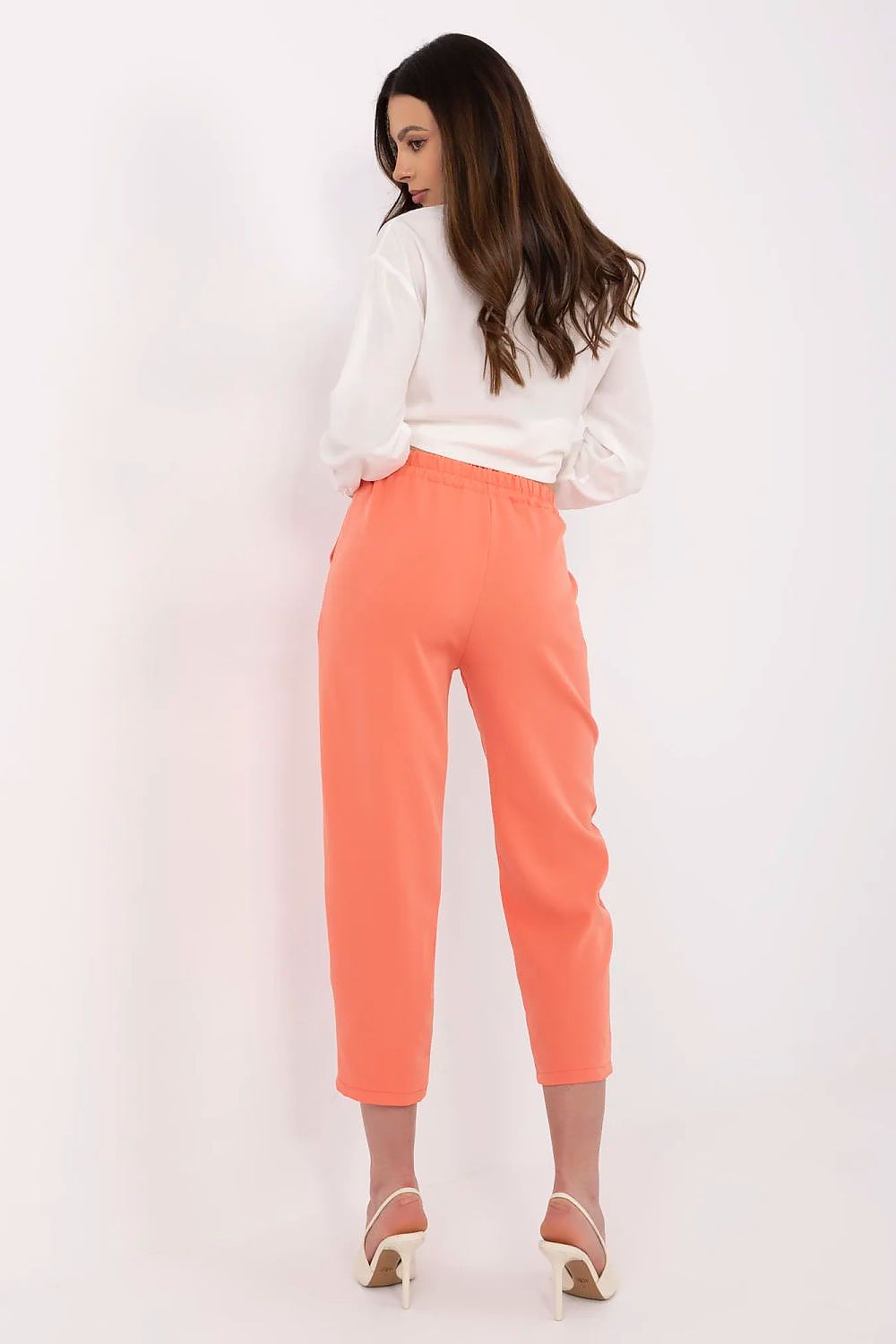 Woman wearing coral pants and a white top on a white background
