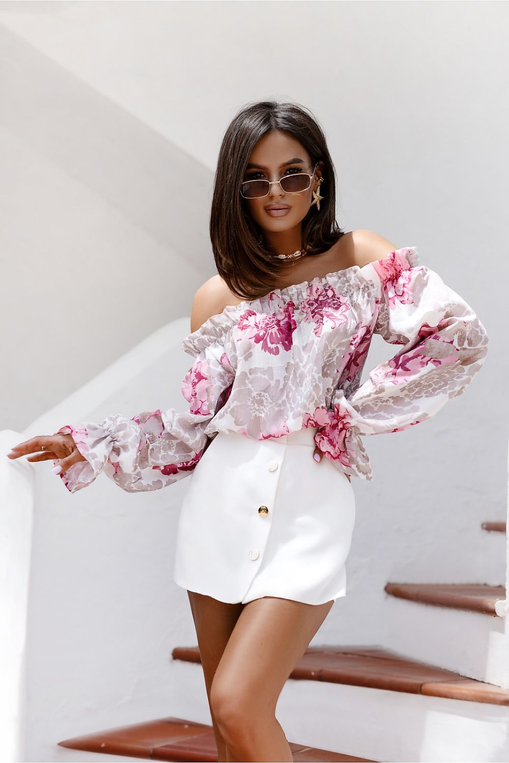 Woman wearing a floral off-shoulder top and white shorts on a staircase.